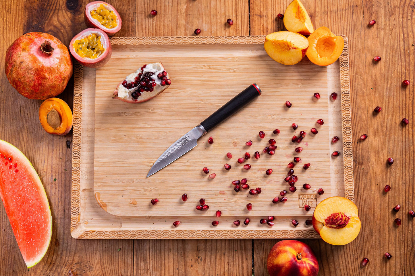 KOTAI paring knife with Tsuchime hammered blade on cutting board among watermelon, pomegranate, and peaches.