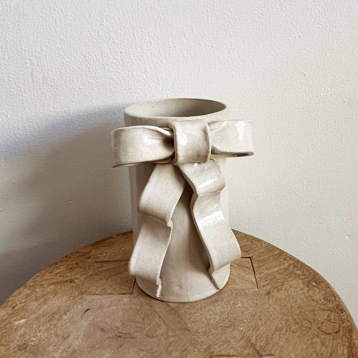 Handmade satin white glazed stoneware vase with a sculpted ribbon bow. Cylindrical ceramic vase adds whimsical charm to floral arrangements.