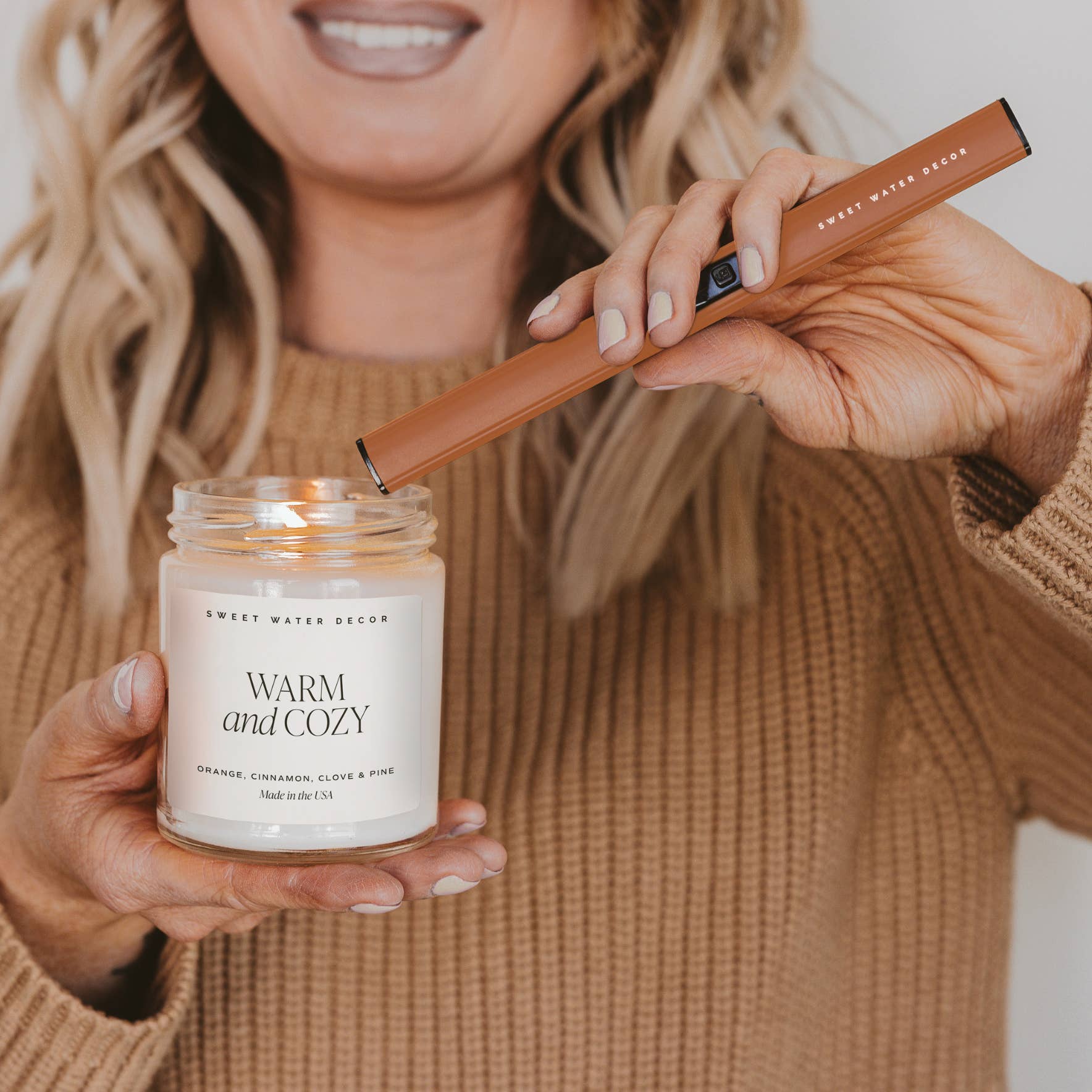 Burnt Orange Rechargeable Electric Lighter held over a Warm and Cozy candle for flameless, eco-friendly ignition.
