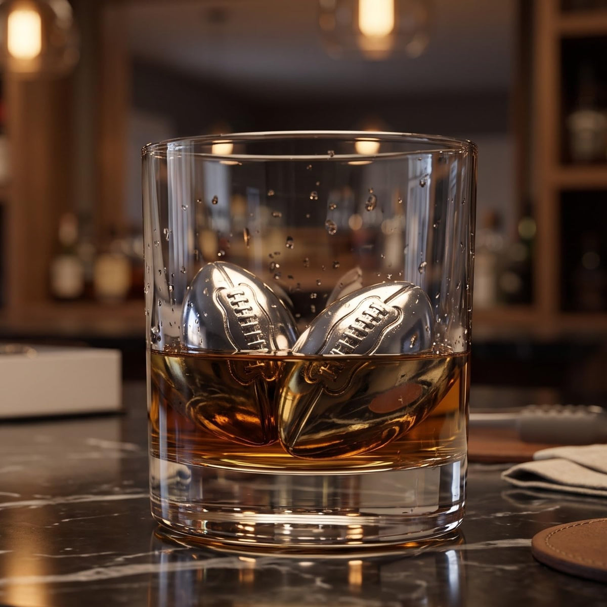 Stainless steel football whiskey stones chilling amber spirits in a glass without dilution. Reusable Superbowl chillers for men.
