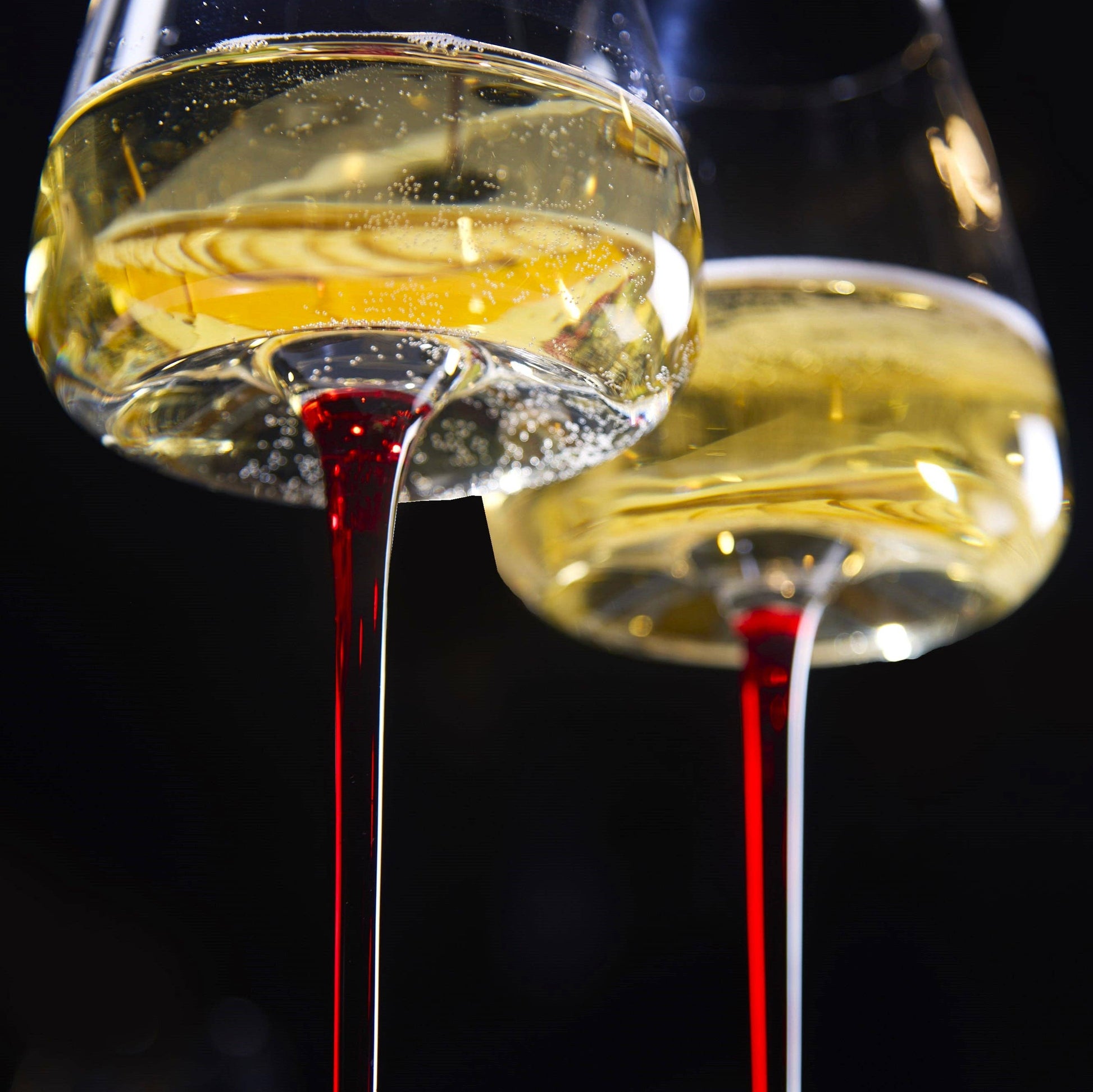 Two large concave wine glasses with ombre red stems, amber wine, 16oz capacity.