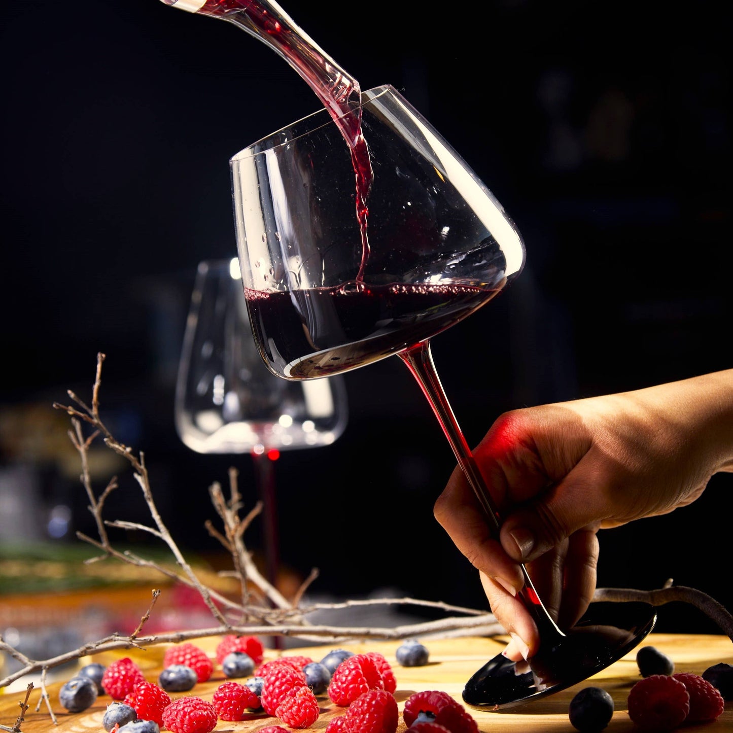 Extra Large Concave 24oz wine glass being filled with red wine, held by stem against a dark background