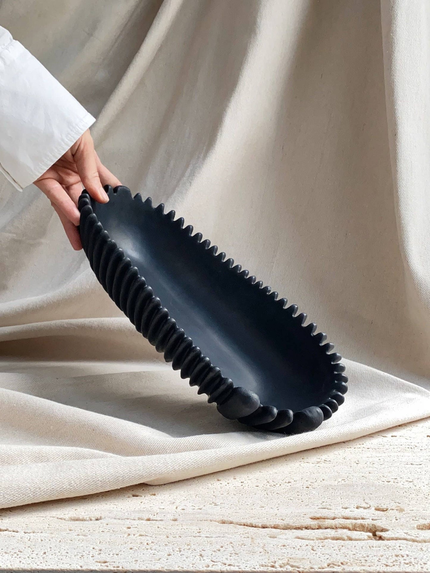 FORMA handmade concrete bowl in black, oval decorative centerpiece, 32x14x7 cm, held by hand.