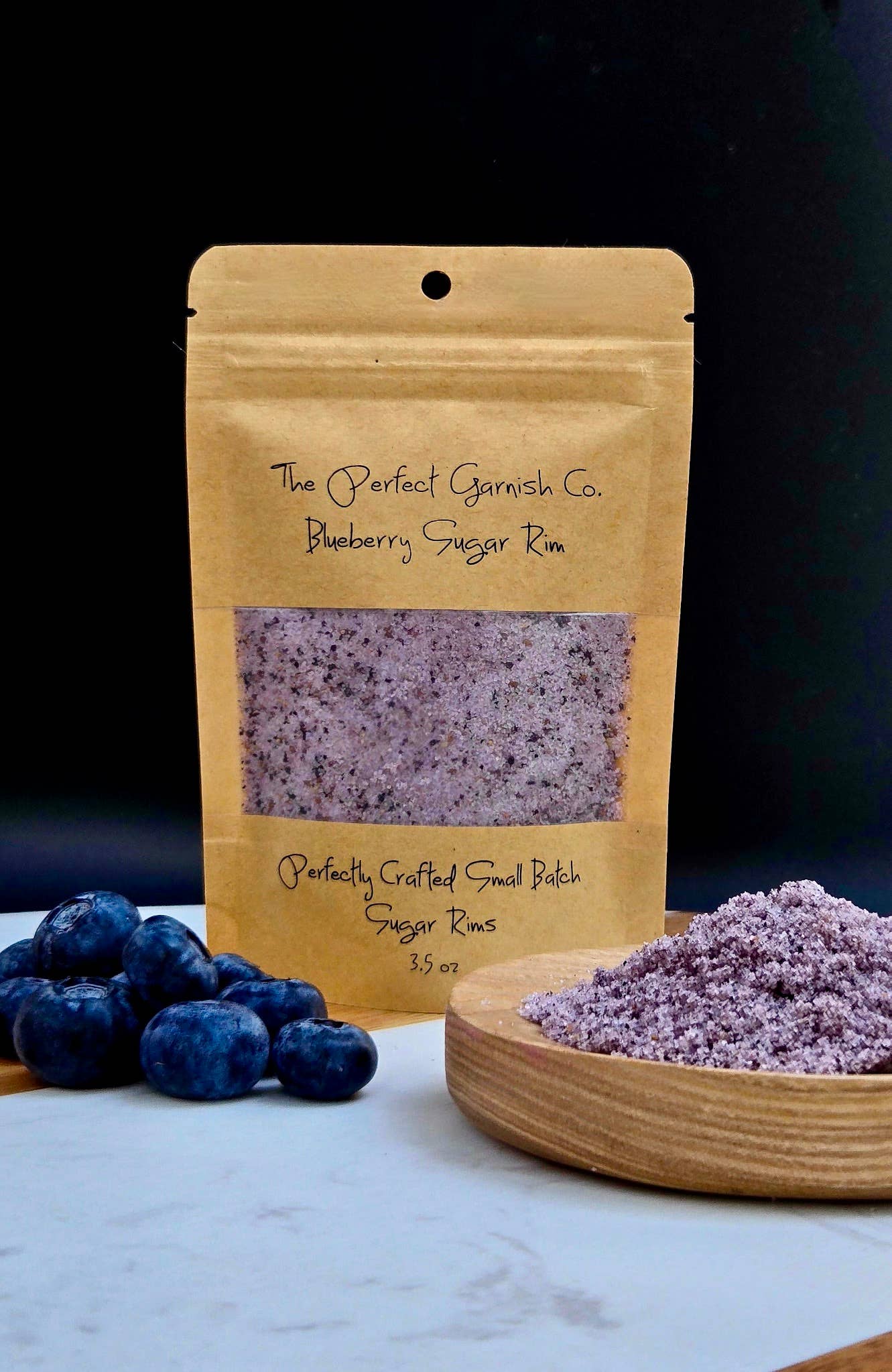 Blueberry Sugar Rim in kraft pouch with purple sugar crystals; blueberries on a white surface.