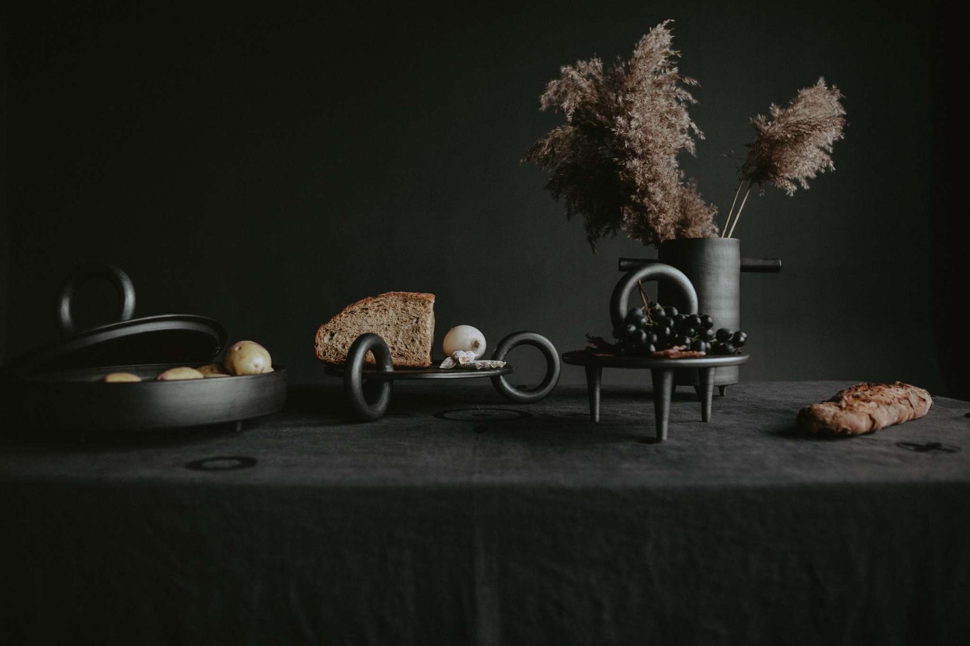 Large Serving Platter Guculia. Trinity with bread, grapes, and a pampas grass vase on a dark table.