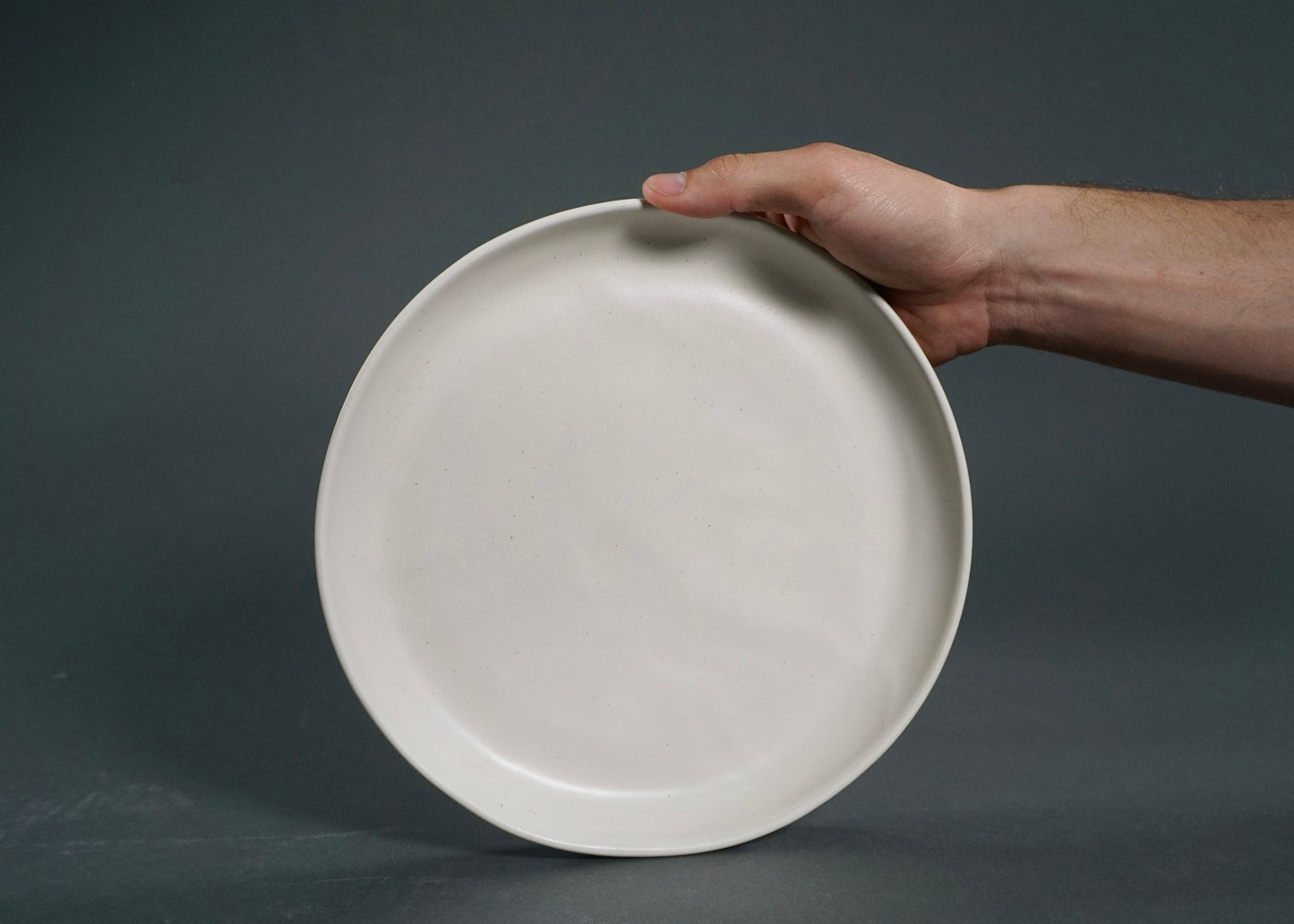 Ivory plate from The Dinnerware Set held by hand, minimalist ceramic.