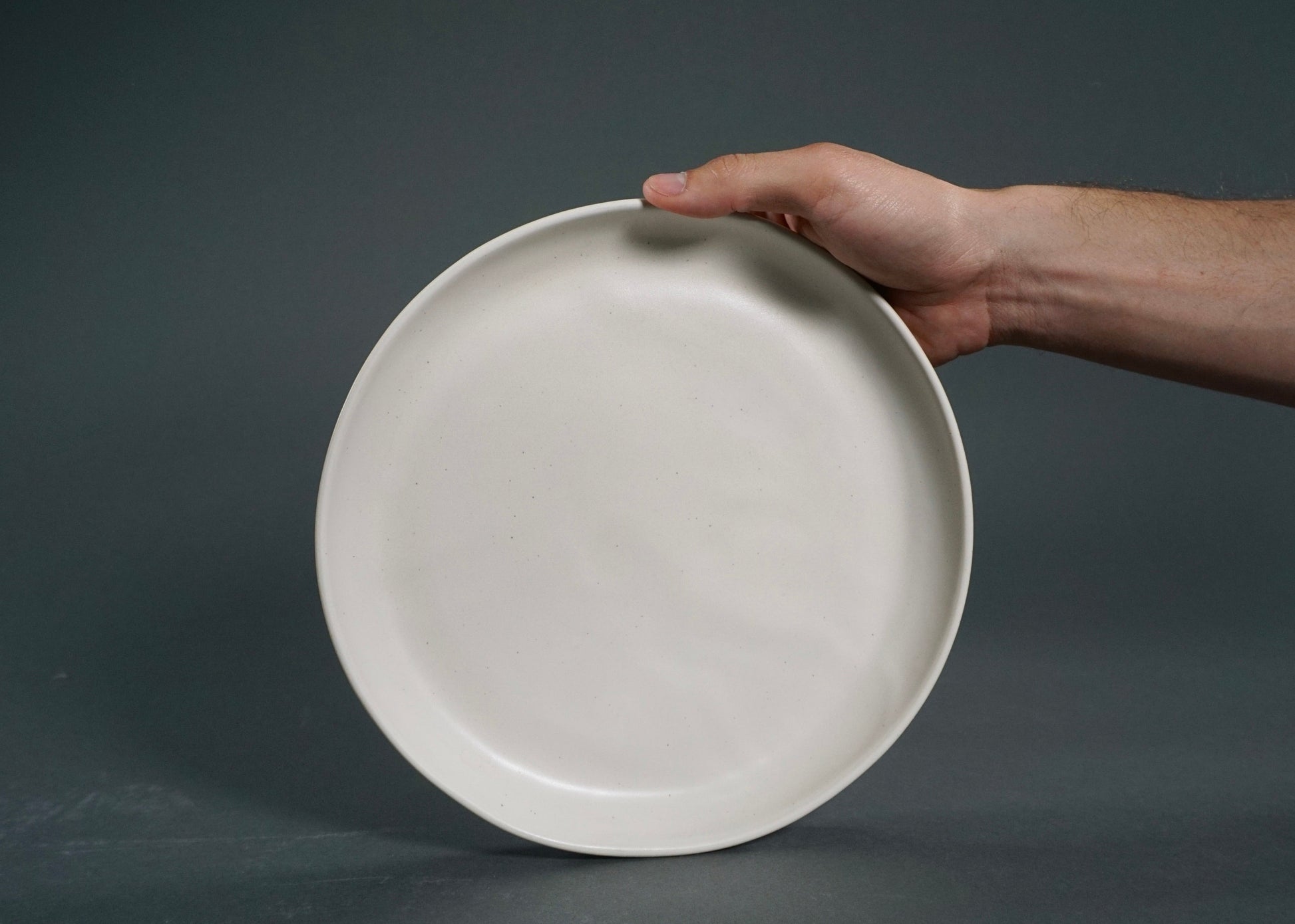 Ivory dinner plate from The Dinnerware Set - Ivory, held by hand.