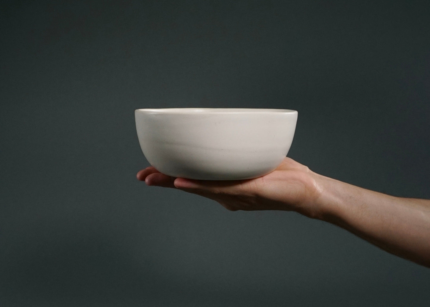 Ivory dinnerware bowl from The Dinnerware Set - Ivory, held in a hand against a dark background.