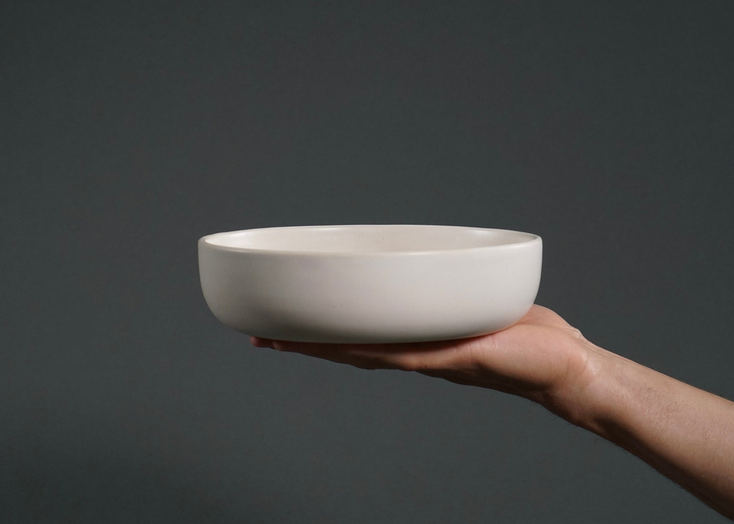 Ivory ceramic dinner bowl held by a hand, part of The Dinnerware Set.