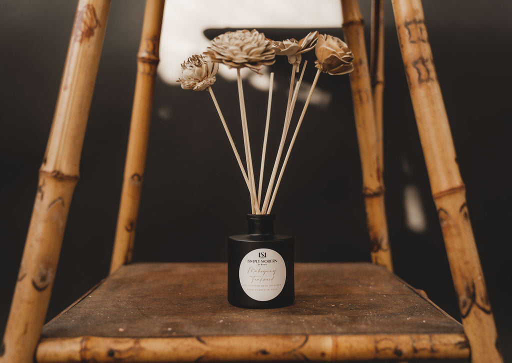 Handmade Floral Reeds diffuser reeds in a black bottle with dried-flower stems on a wooden chair.