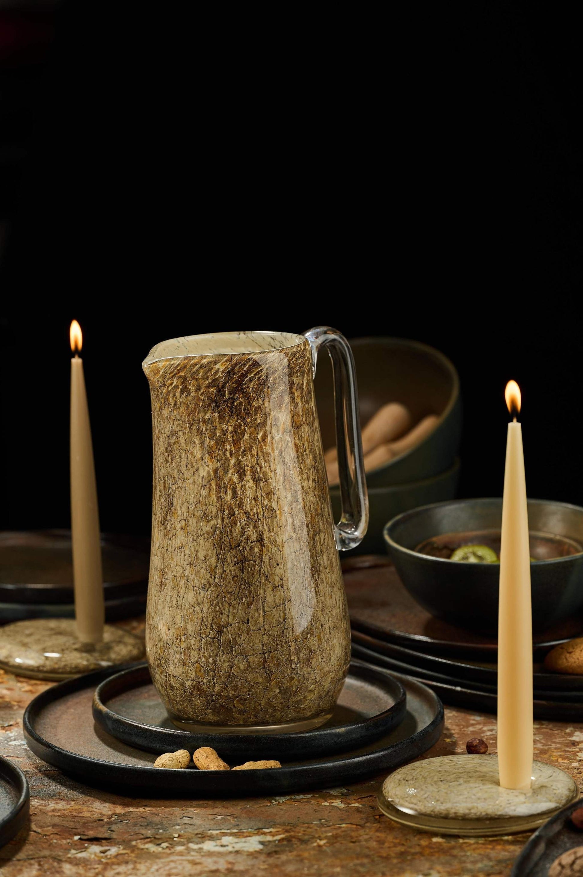 Hand blown glass pitcher with round shape and marble-inspired pattern, clear handle, in a candlelit setting.
