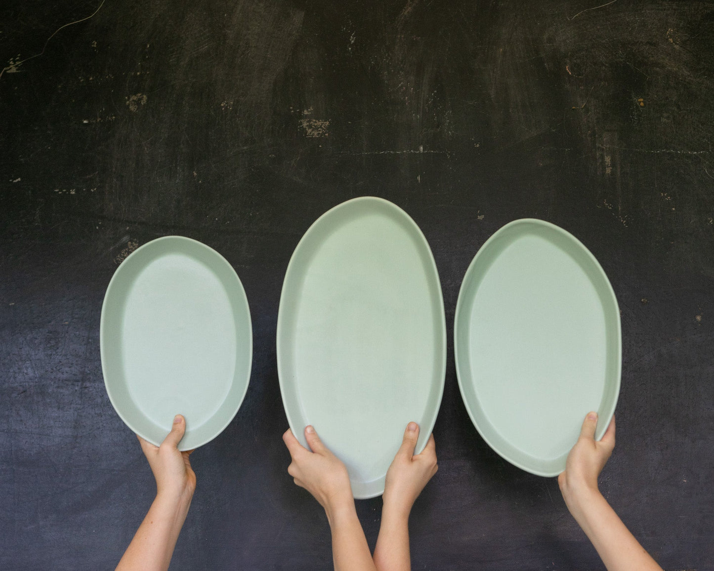 Three-piece mint-green oval serving platters in 13, 15, and 18 inches, held by hands.