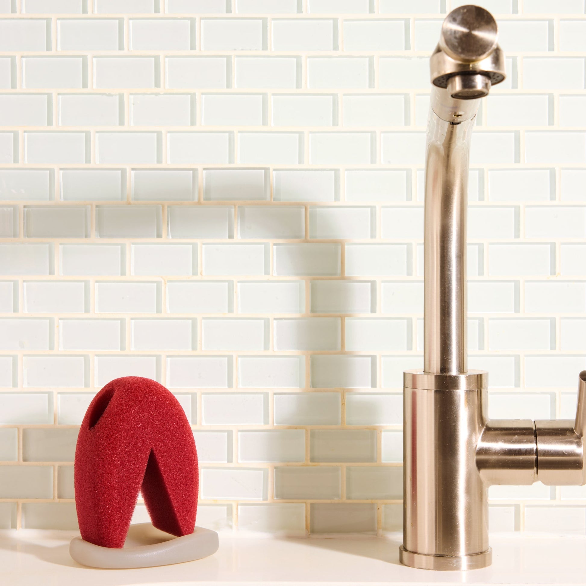 The Starter Kitt ergonomic sponge with base doubles as a ring dish, displayed beside a copper faucet.