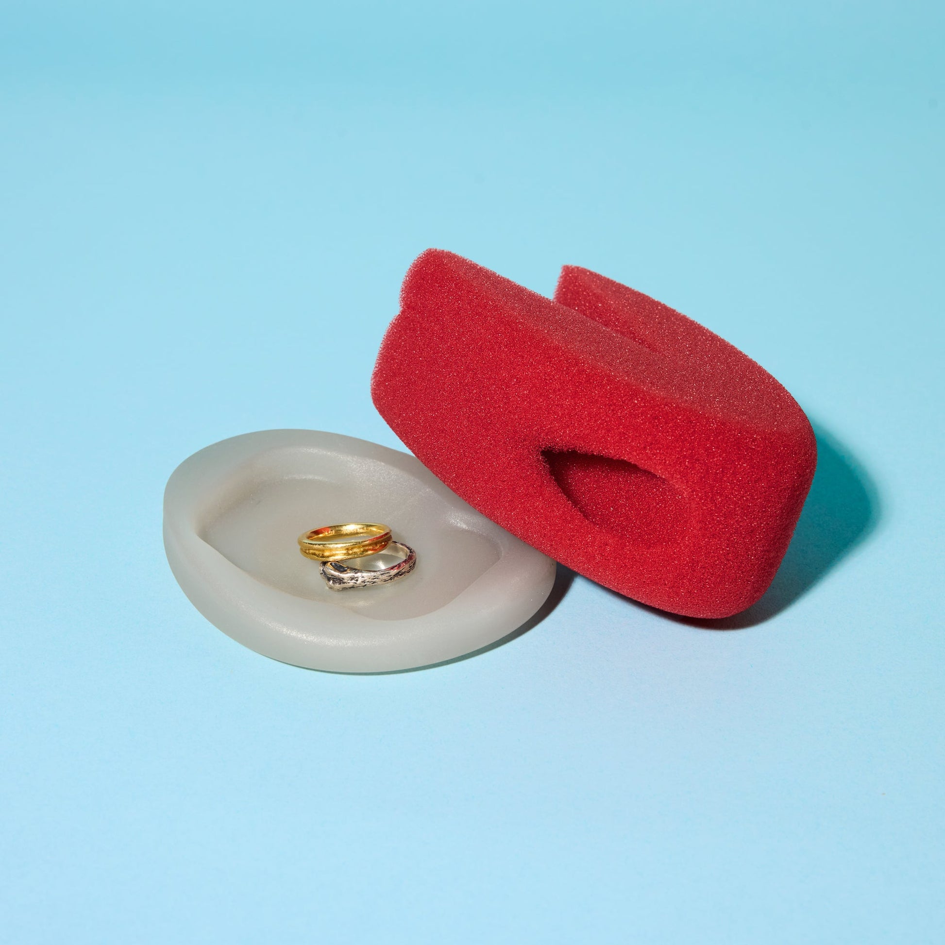 The Starter Kitt red ergonomic sponge for wine glasses with white base that doubles as a ring dish on blue background.