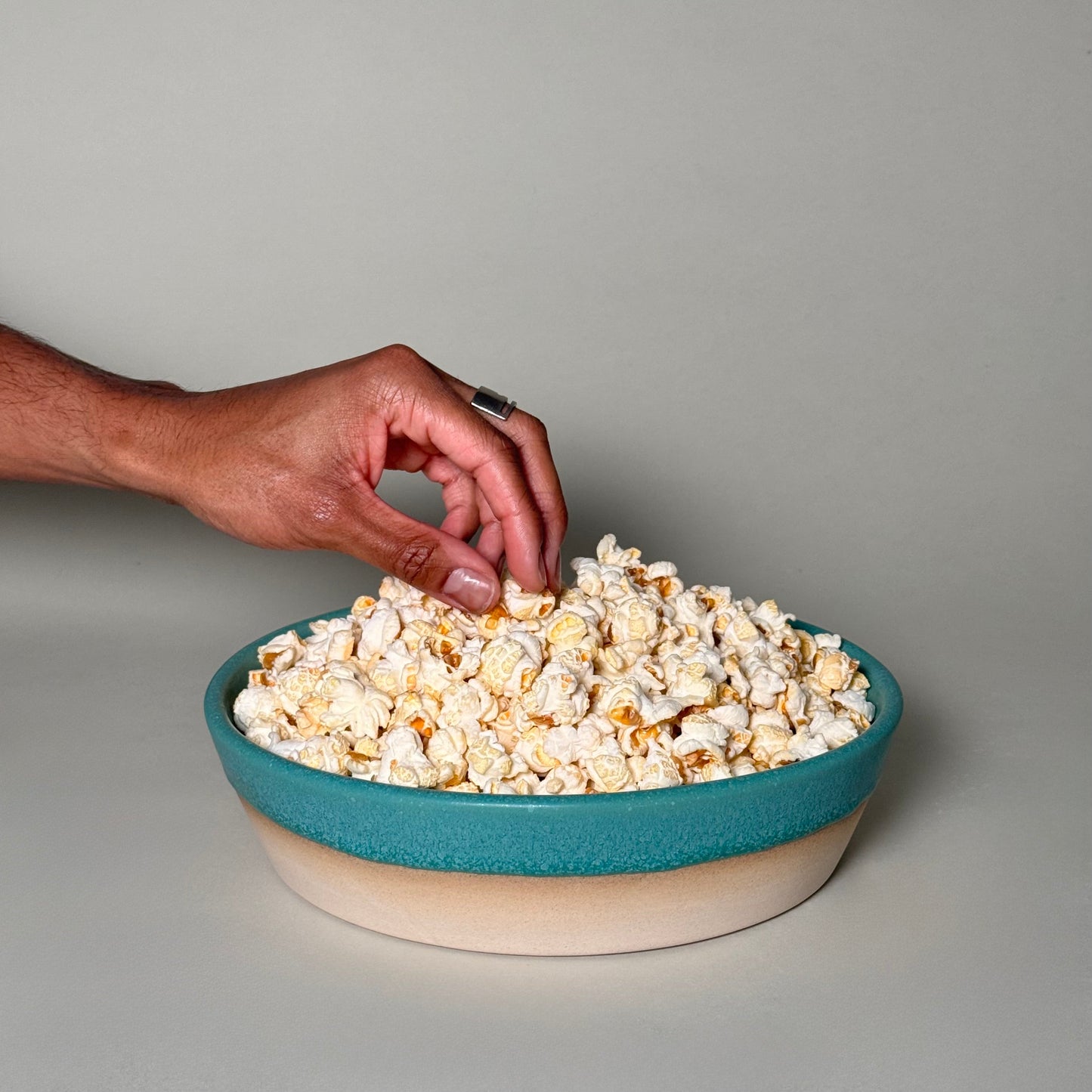 Share Bowl - 9 inch teal bowl with beige base, filled with popcorn as hand reaches in.