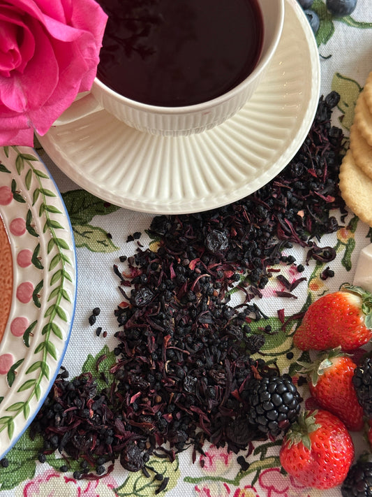 Berry Petal Infusion Herbal Tea: loose hibiscus, currants, and elderberries blend beside a dark cup and fresh berries.