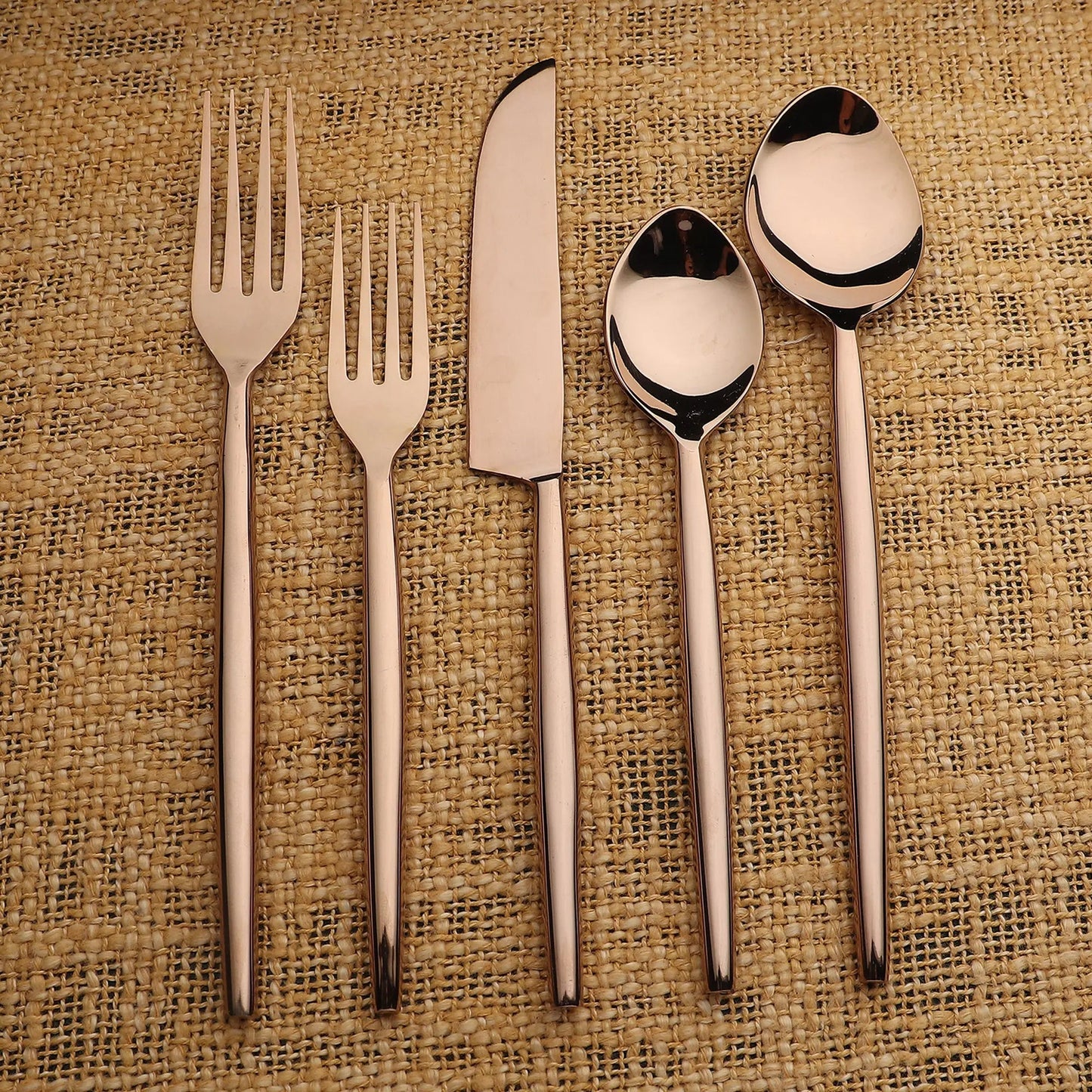 Brio PVD 5-piece flatware set in rose-gold finish with slim elegant handles on burlap background.