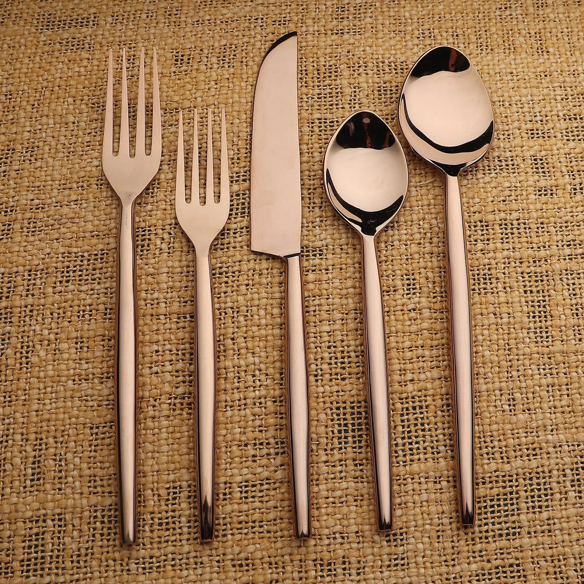 Brio PVD 5-piece flatware set in rose-gold finish with slim elegant handles on burlap background.