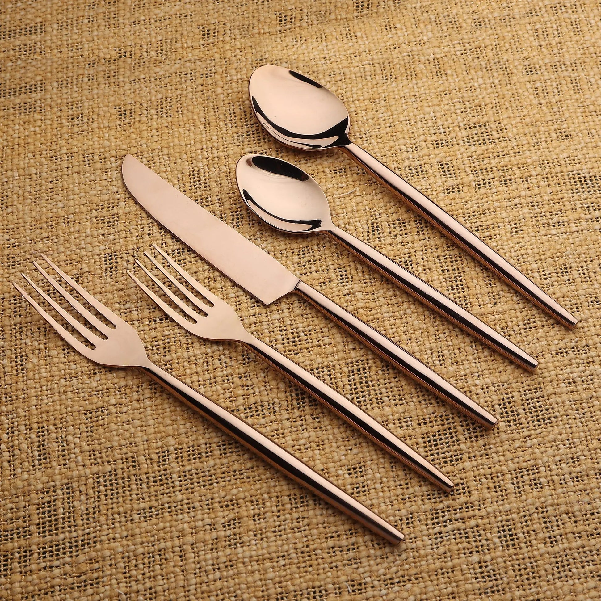 Brio PVD 5 Pc. Flatware Set in rose-gold finish with slim, balanced handles on burlap background.