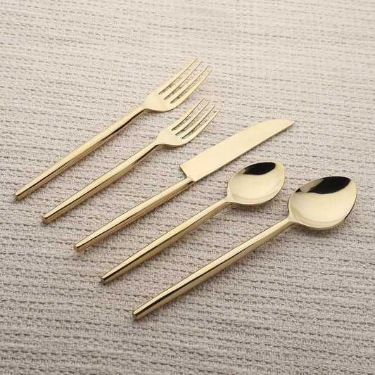 Brio PVD gold 5-piece flatware set with slim tapered handles on beige fabric.
