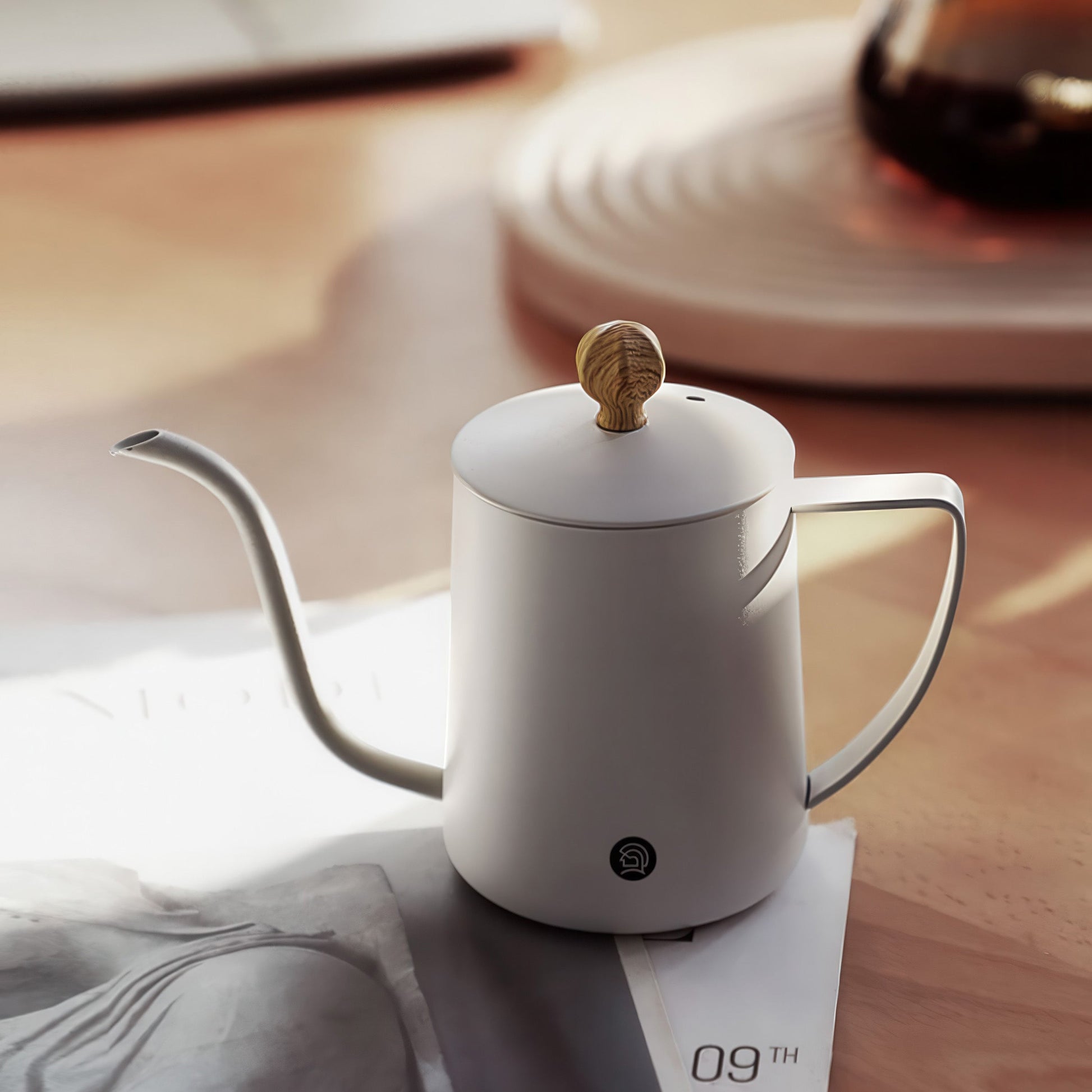 White gooseneck pour-over coffee kettle with wooden knob lid on a table