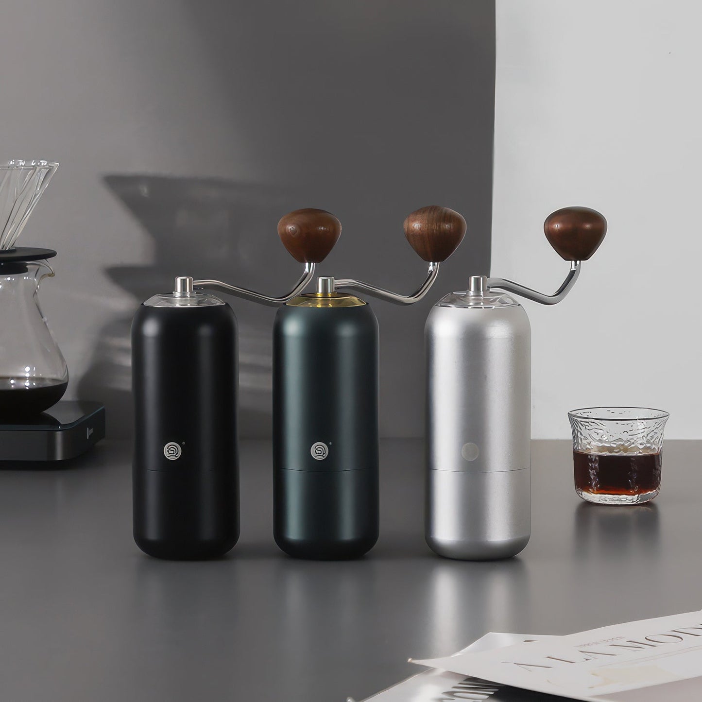 Three Z7 manual coffee grinders for pour-over in black, green, and silver with wooden handles on a countertop.