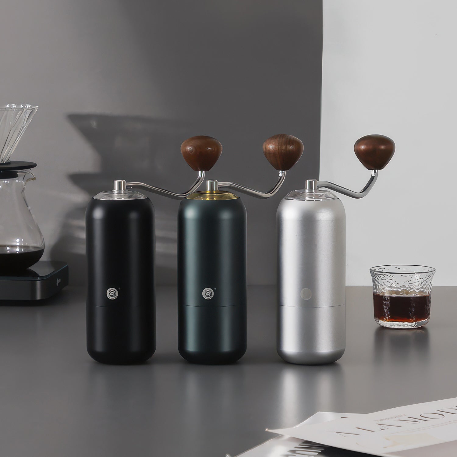 Three Z7 manual coffee grinders for pour-over in black, green, and silver with wooden handles on a countertop.