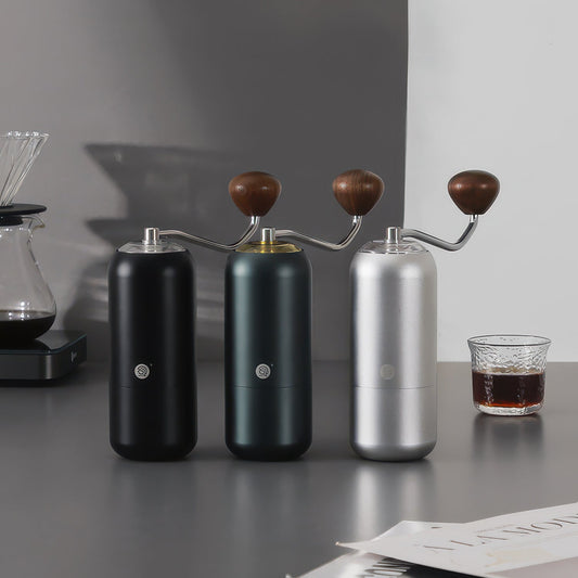Three Z7 manual coffee grinders for pour-over in black, green, and silver with wooden handles on a countertop.