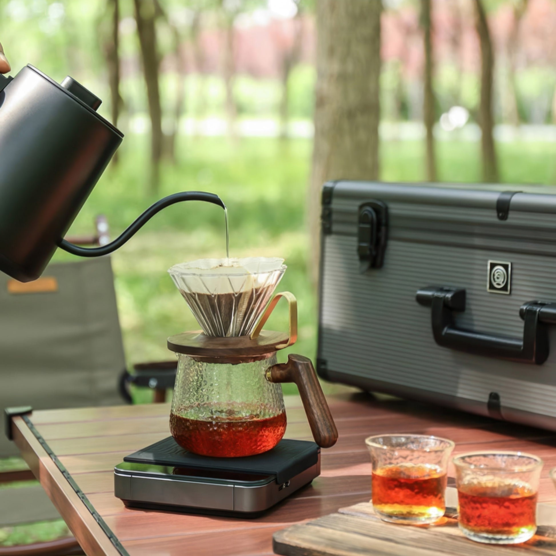 Ultimate Pour Over Coffee Pro Kit: outdoor setup with gooseneck kettle, dripper over glass carafe, and travel case.