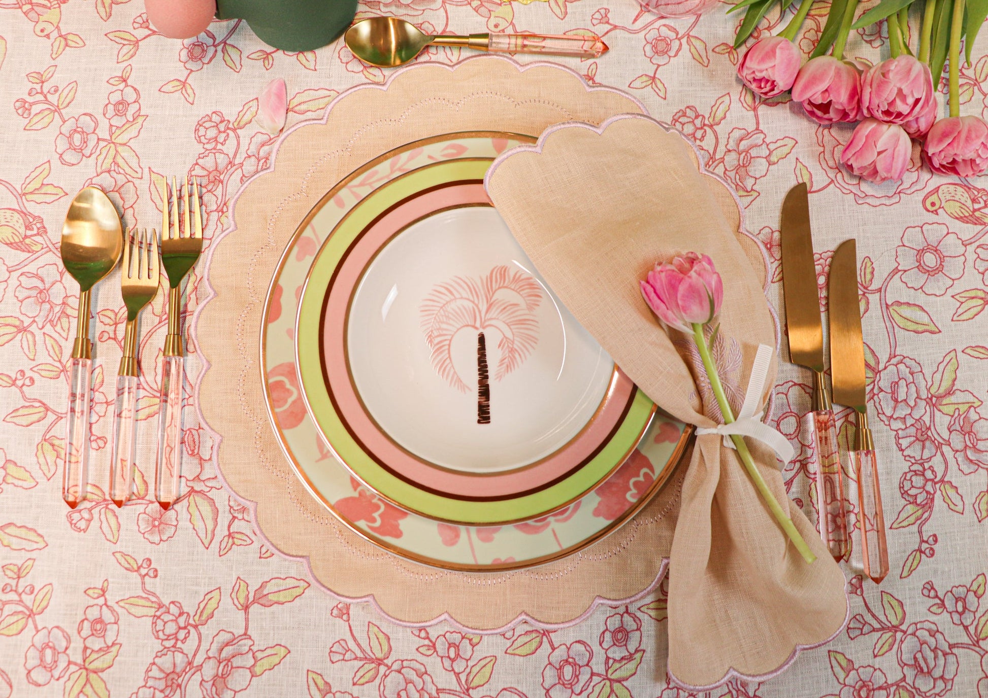 Peony Blush gold-toned cutlery with rose-petal handles beside pastel plates and pink roses on a floral table setting.
