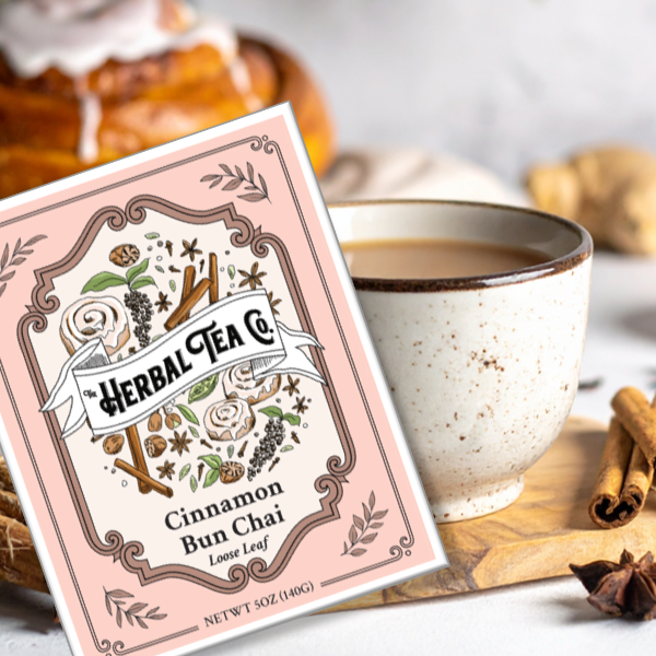 Herbal Tea Co Cinnamon Bun Chai packaging beside a mug of chai with cinnamon sticks.