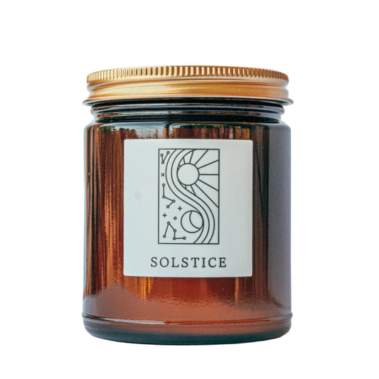 Solstice Fine Fragrance Candle in amber jar with SOLSTICE label and sun–moon graphic.