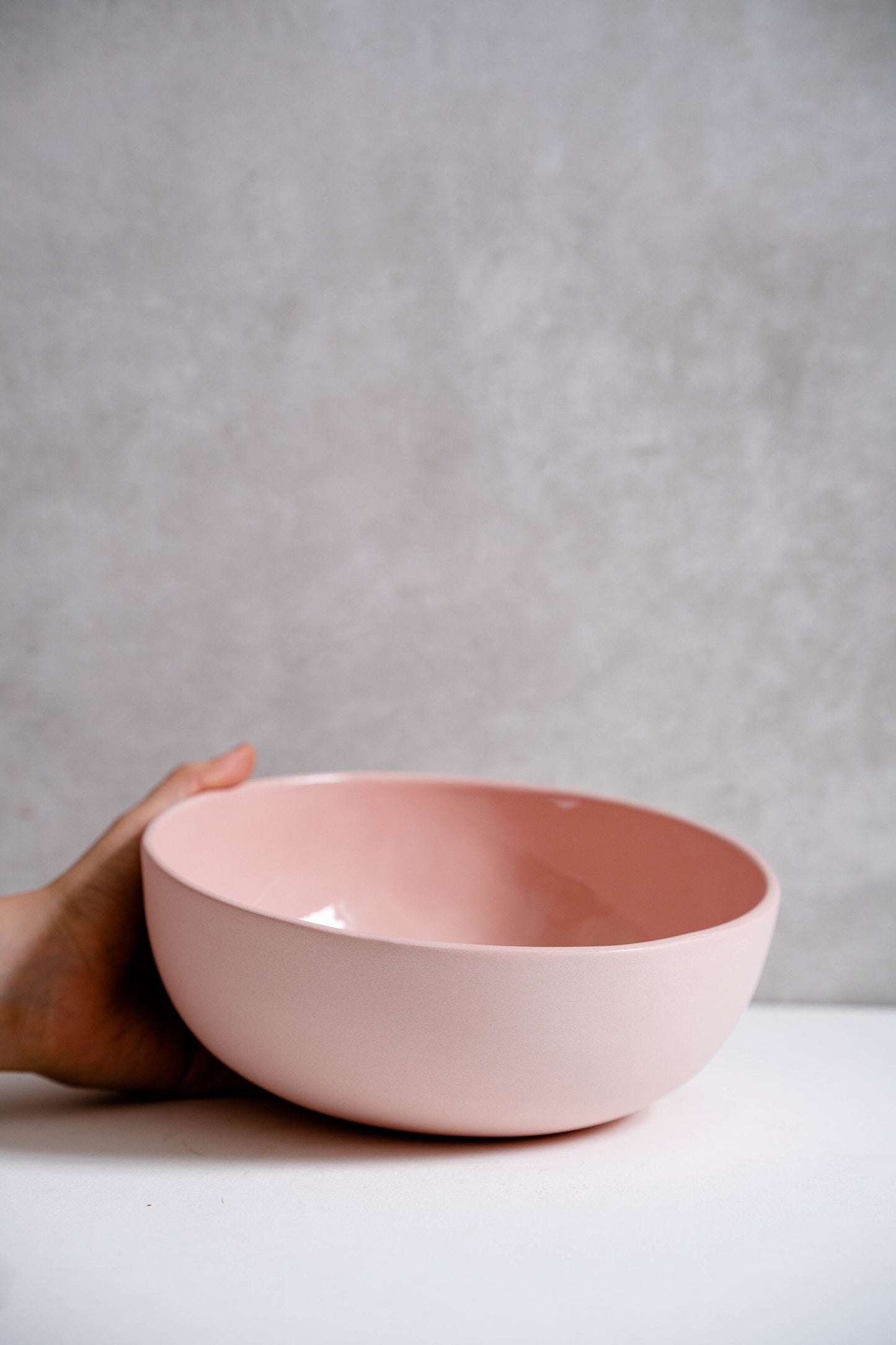 Powder Pink Handmade Porcelain Salad Serving Bowl held by hand on a white table.
