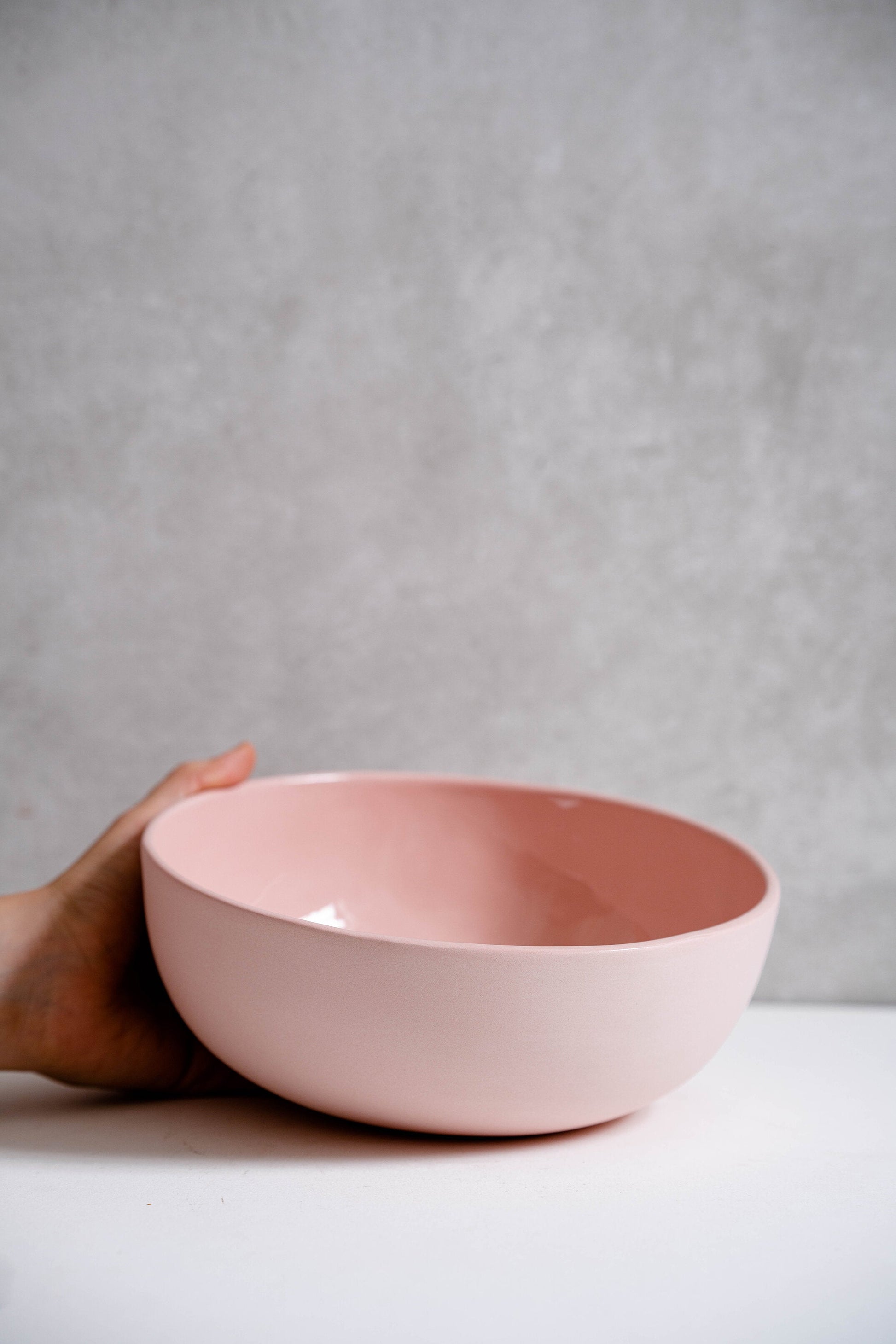 Powder Pink Handmade Porcelain Salad Serving Bowl held by hand on a white table.