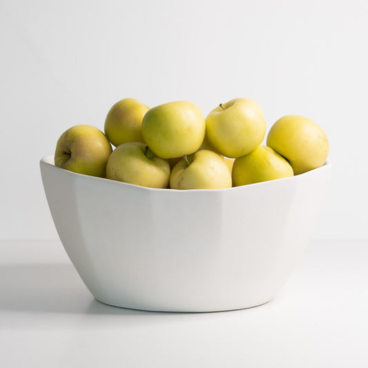 Large white porcelain nesting bowl filled with yellow-green apples.