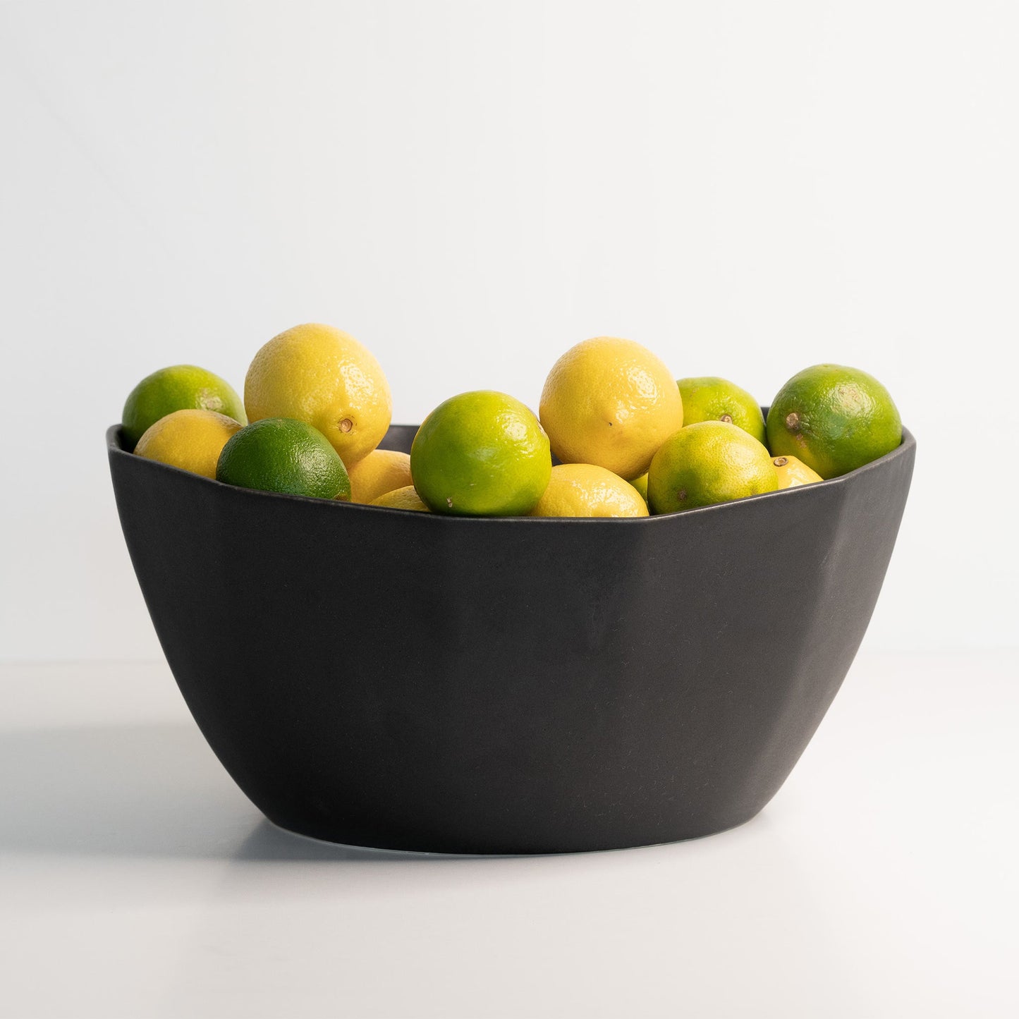 Matte black porcelain nesting bowl filled with lemons and limes.