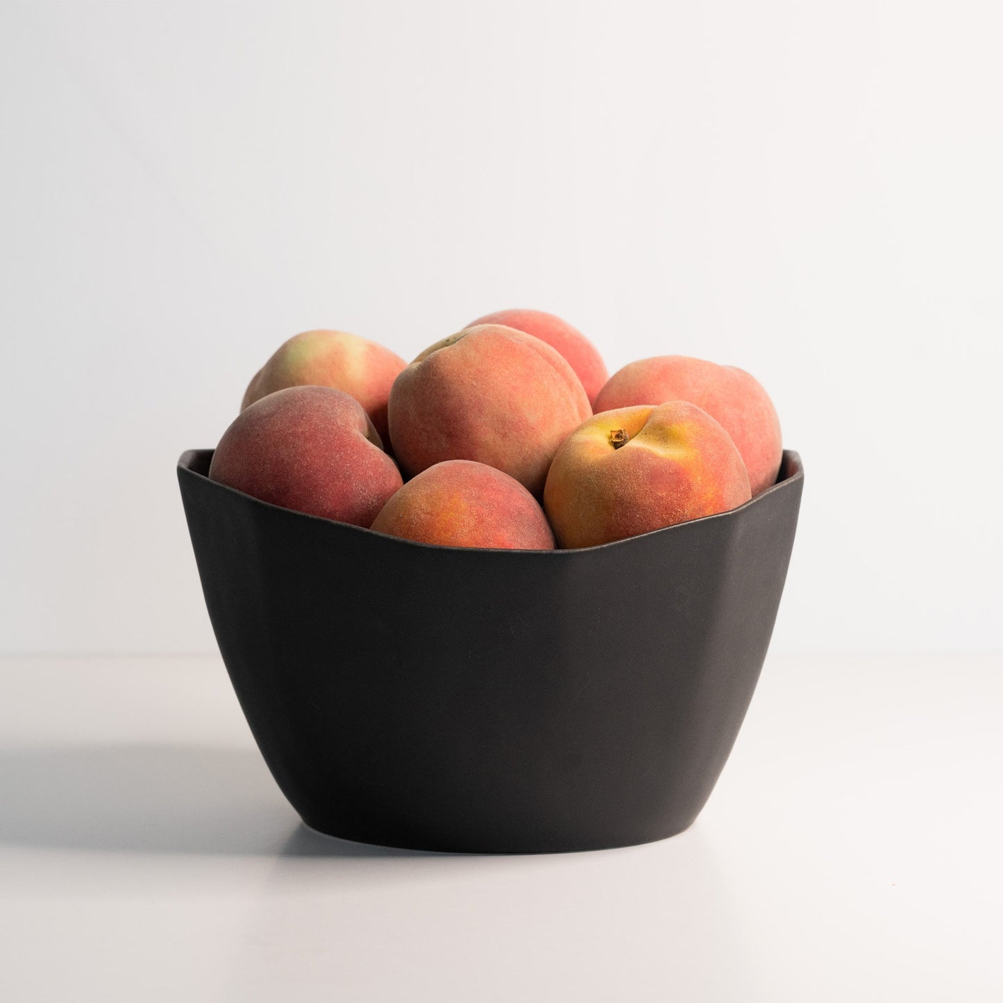 Ember Collective’s Medium Porcelain Nesting Bowl in matte black, filled with peaches.