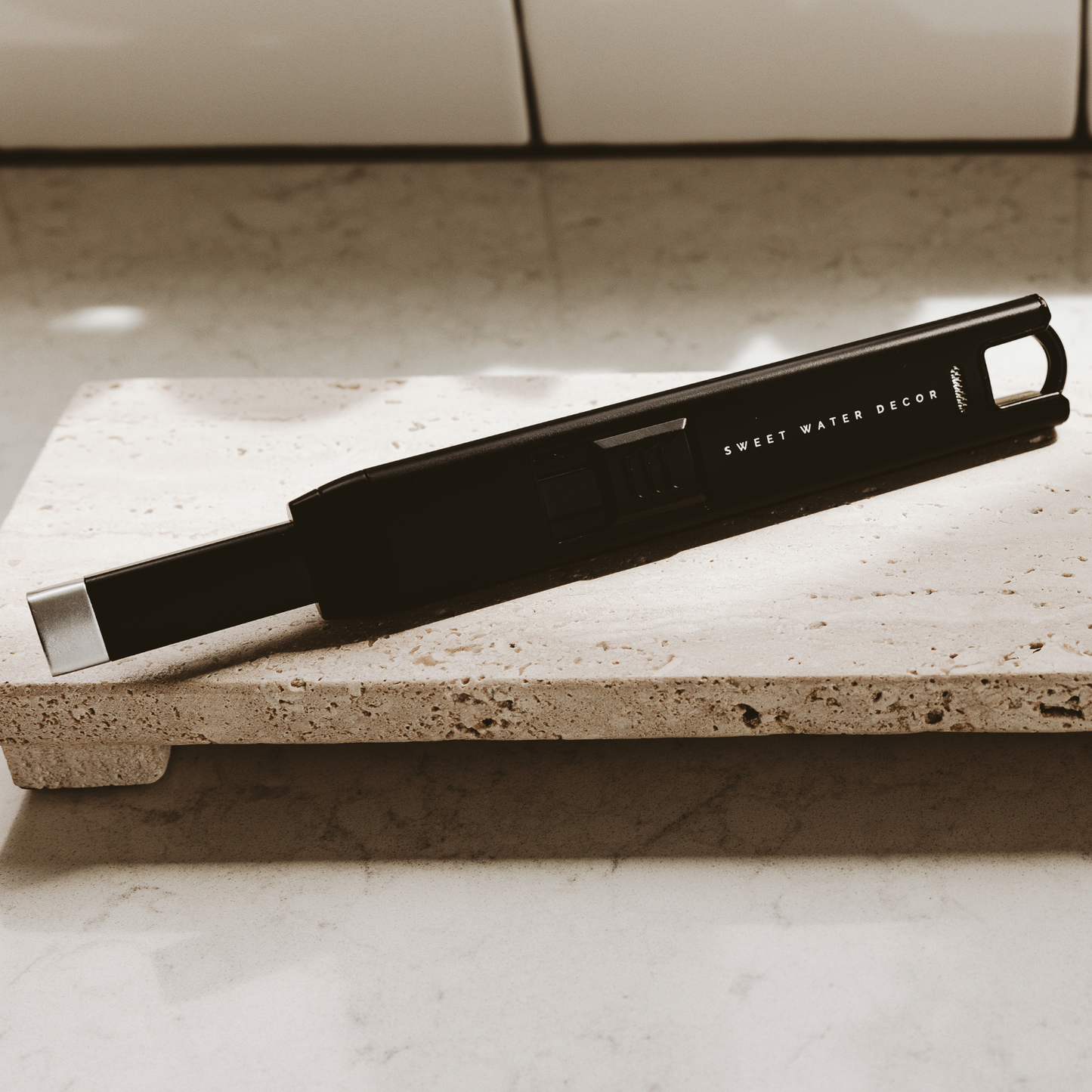 Black large rechargeable electric lighter with ergonomic grip resting on a beige stone countertop.