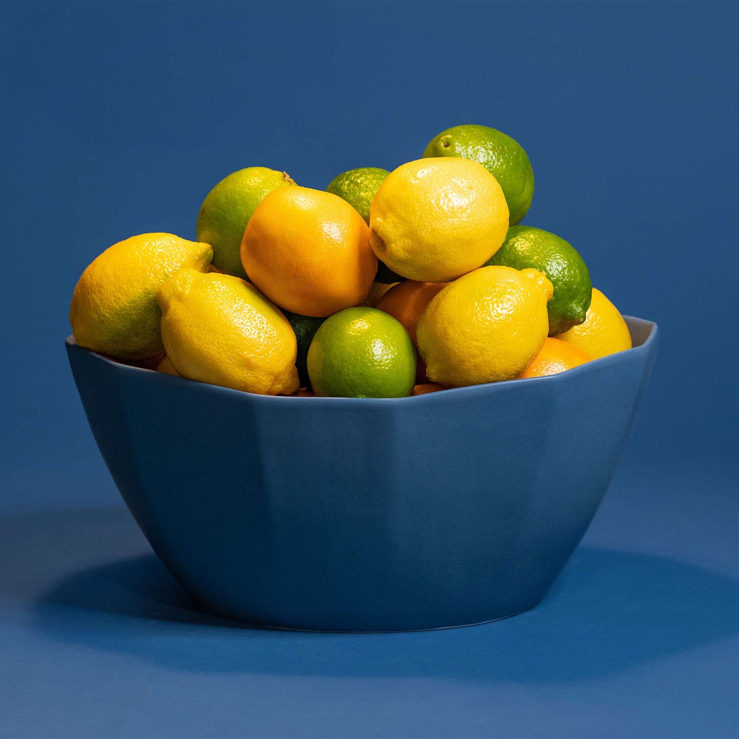 Large porcelain nesting bowl filled with lemons and limes on a blue backdrop.