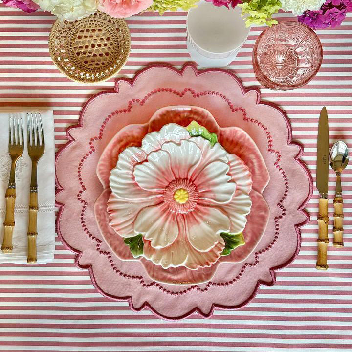 Harmony pink round fabric placemat with scalloped edge, beneath a floral plate on a pink-striped table.