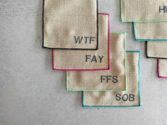 Set of 8 colorful-edged cocktail coasters with letters spelling swear words.