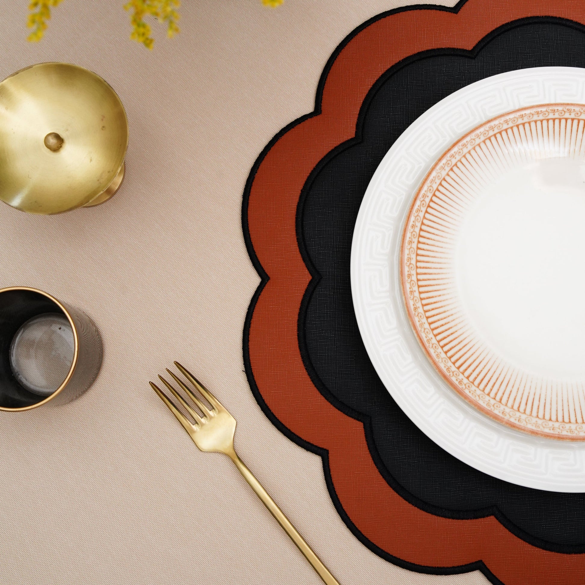 Round scalloped faux leather placemat in black and orange beneath a white patterned plate on a beige table.